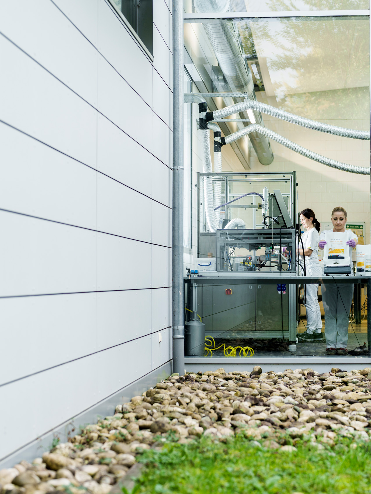 Blick von außen in die Becht-Produktion mit Mitarbeitenden an einer modernen Fertigungsanlage hinter Glas.